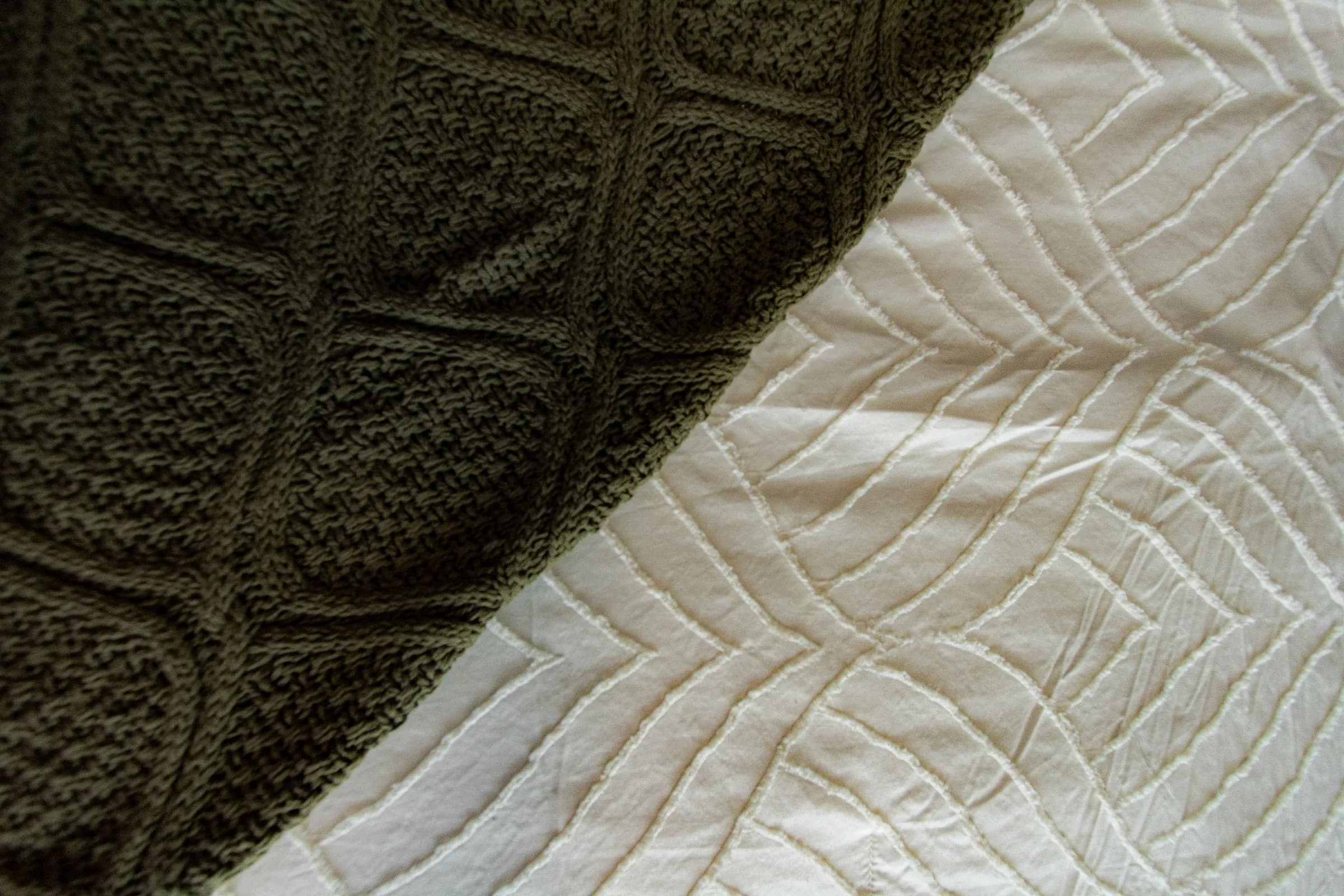 Detalhe da manta de tricô verde-oliva sobre colcha off-white com relevo de folhas