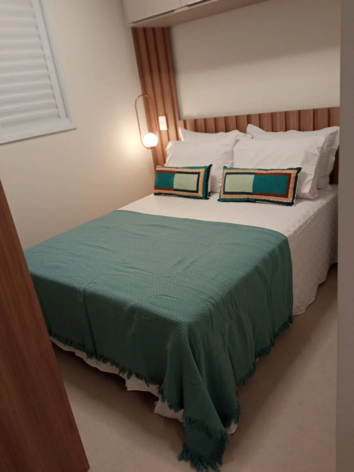 Quarto de casal com manta verde-petróleo e cabeceira de madeira ripada