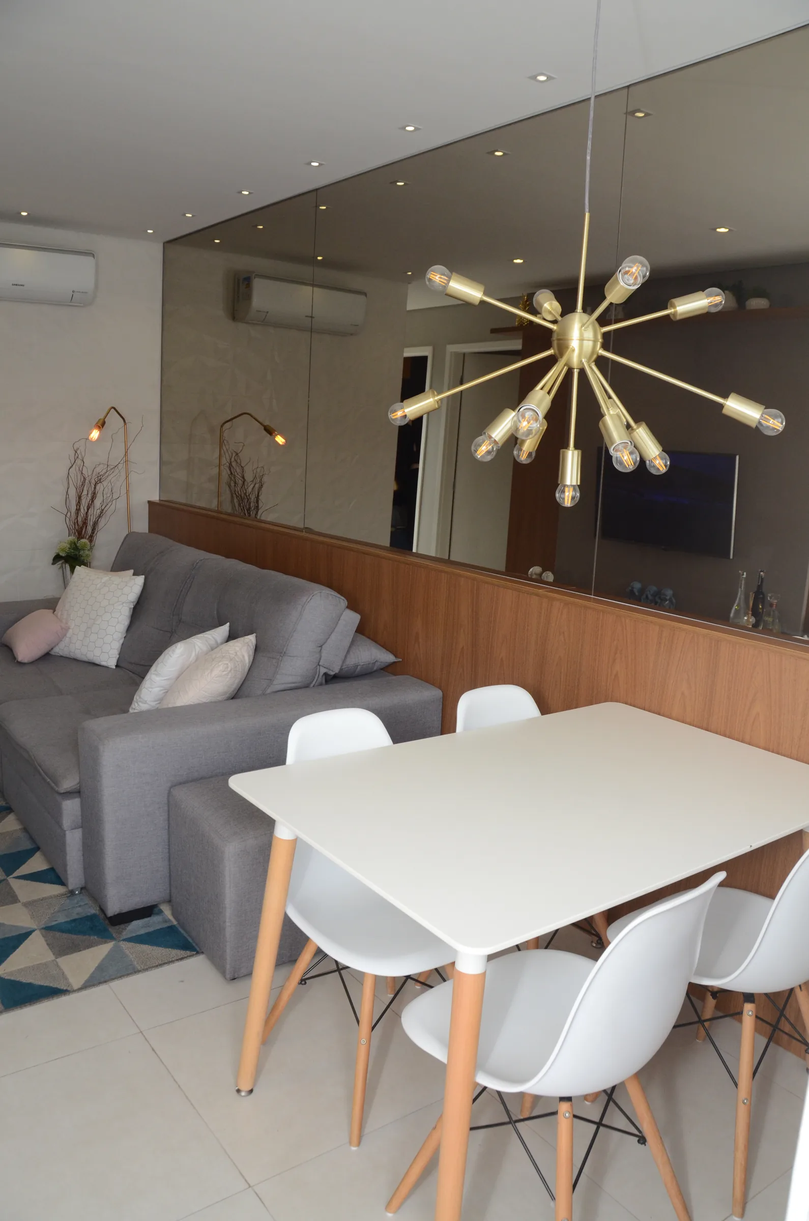 Mesa de jantar branca e lustre sputnik dourado diante da parede espelhada