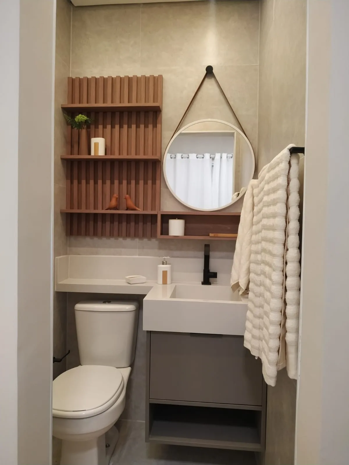 Lavabo com prateleira ripada terracota, espelho redondo com alça e toalha de textura