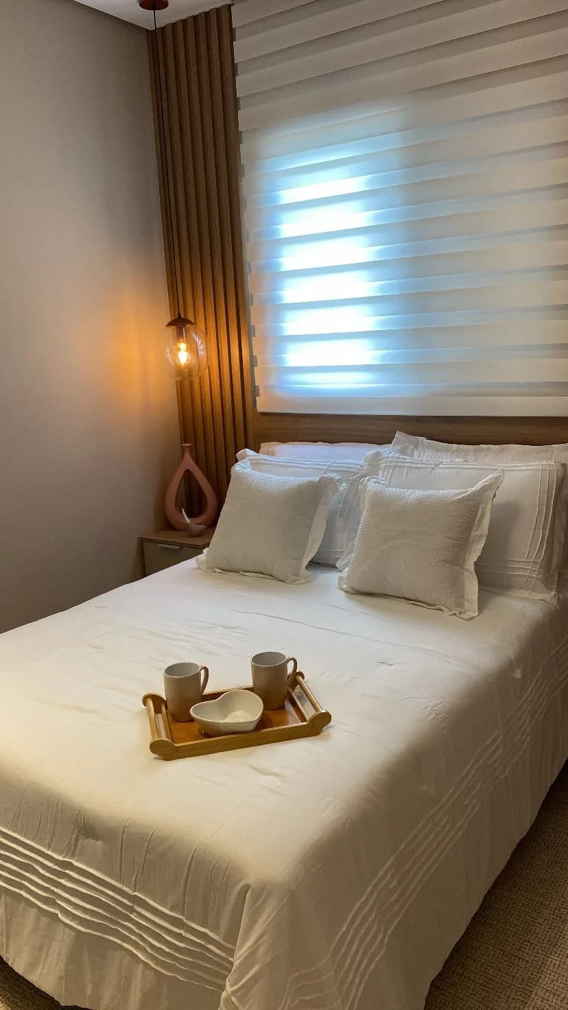 Quarto de casal com cama branca, bandeja de café e pendente âmbar
