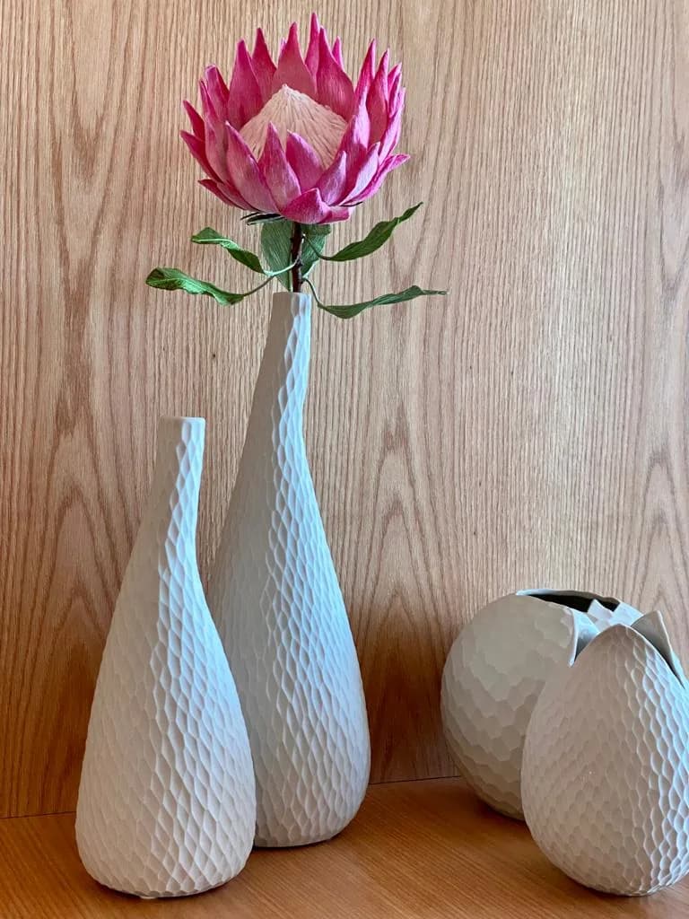 Vasos cerâmicos brancos texturizados e protea rosa contra fundo de madeira