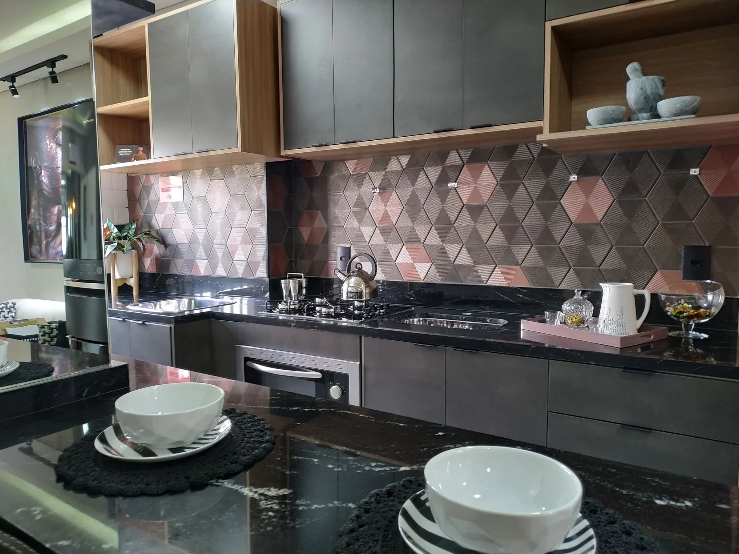 Cozinha grafite com revestimento hexagonal rosado e bowls brancos sobre granito preto