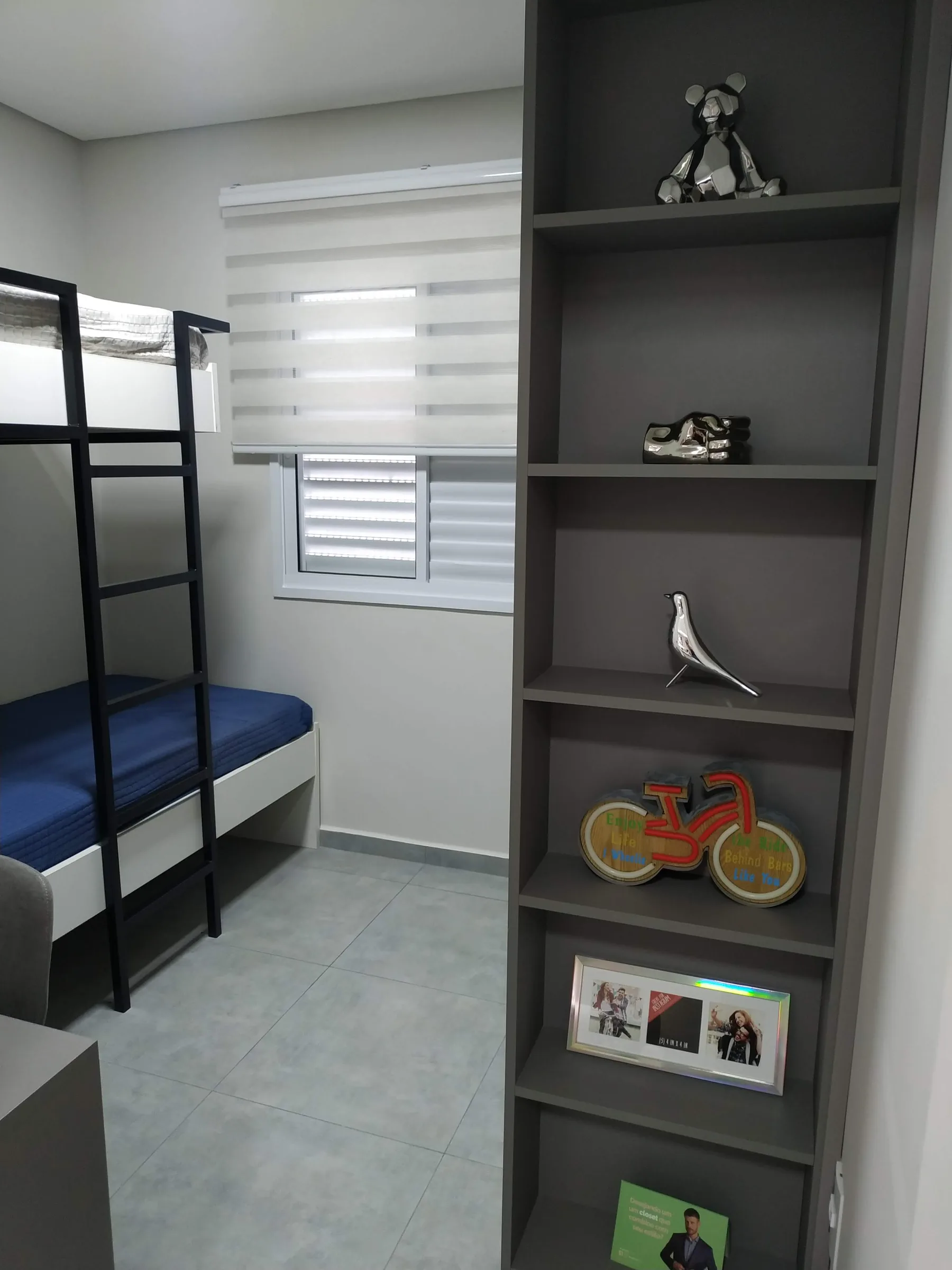 Estante estreita com objetos lúdicos, bicicleta decorativa e beliche ao fundo