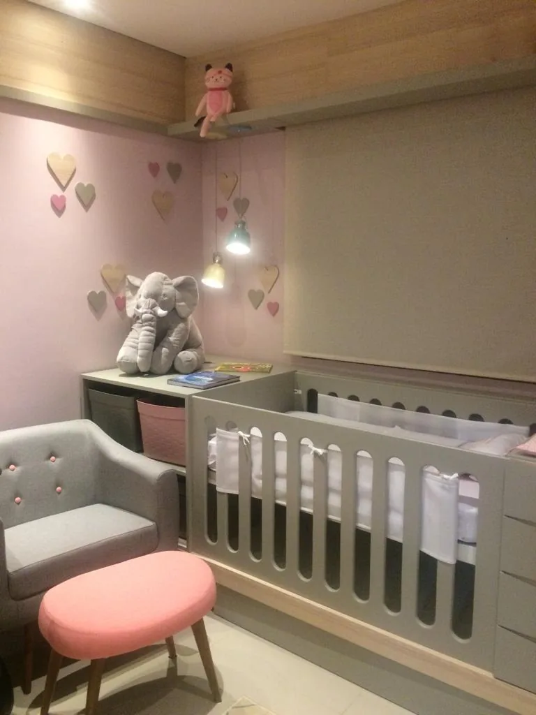 Quarto de bebê com poltrona cinza, pufe rosa, berço cinza e corações de madeira na parede