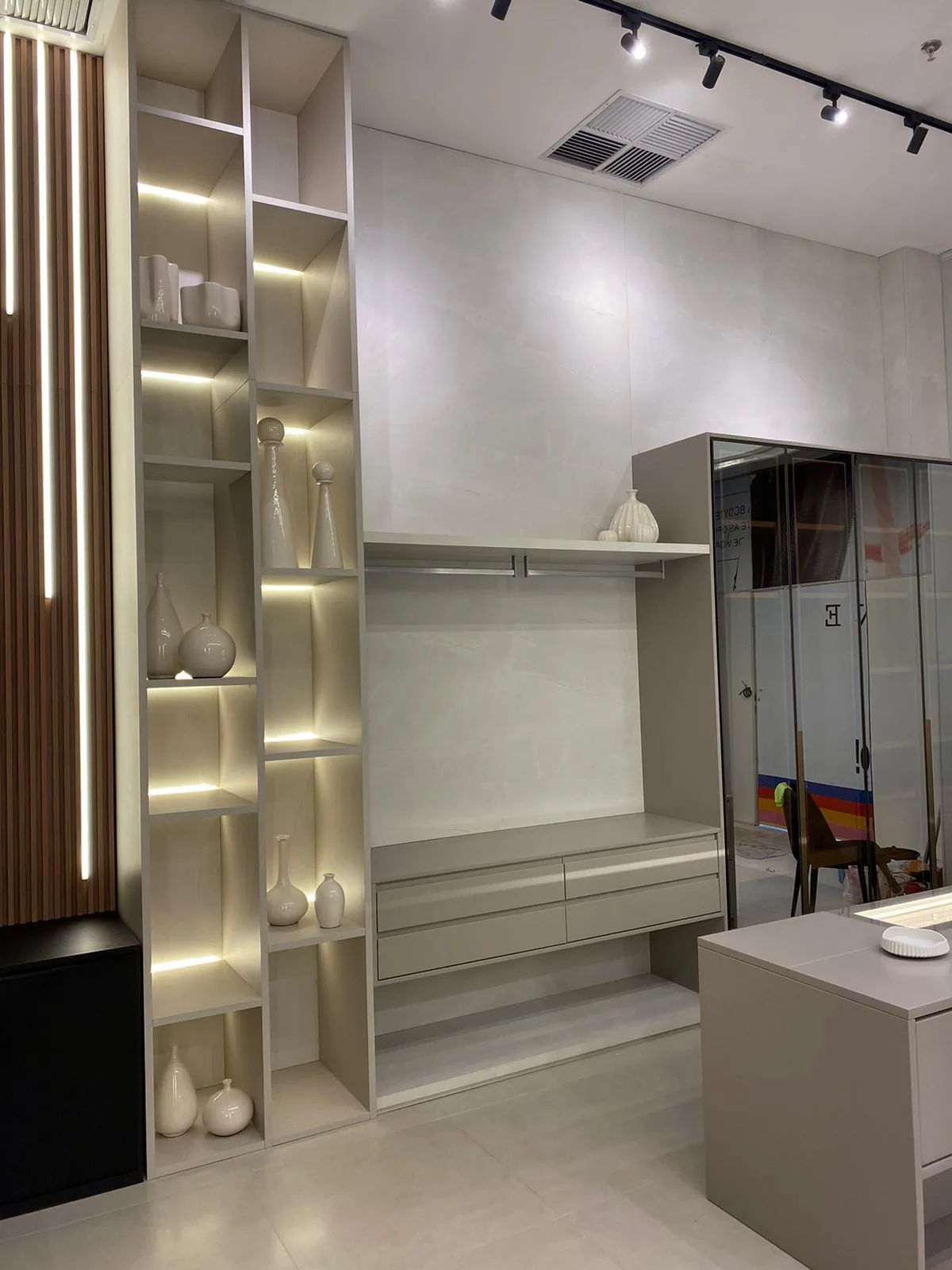 Estante alta com nichos iluminados, vasos de cerâmica clara e móvel suspenso cinza