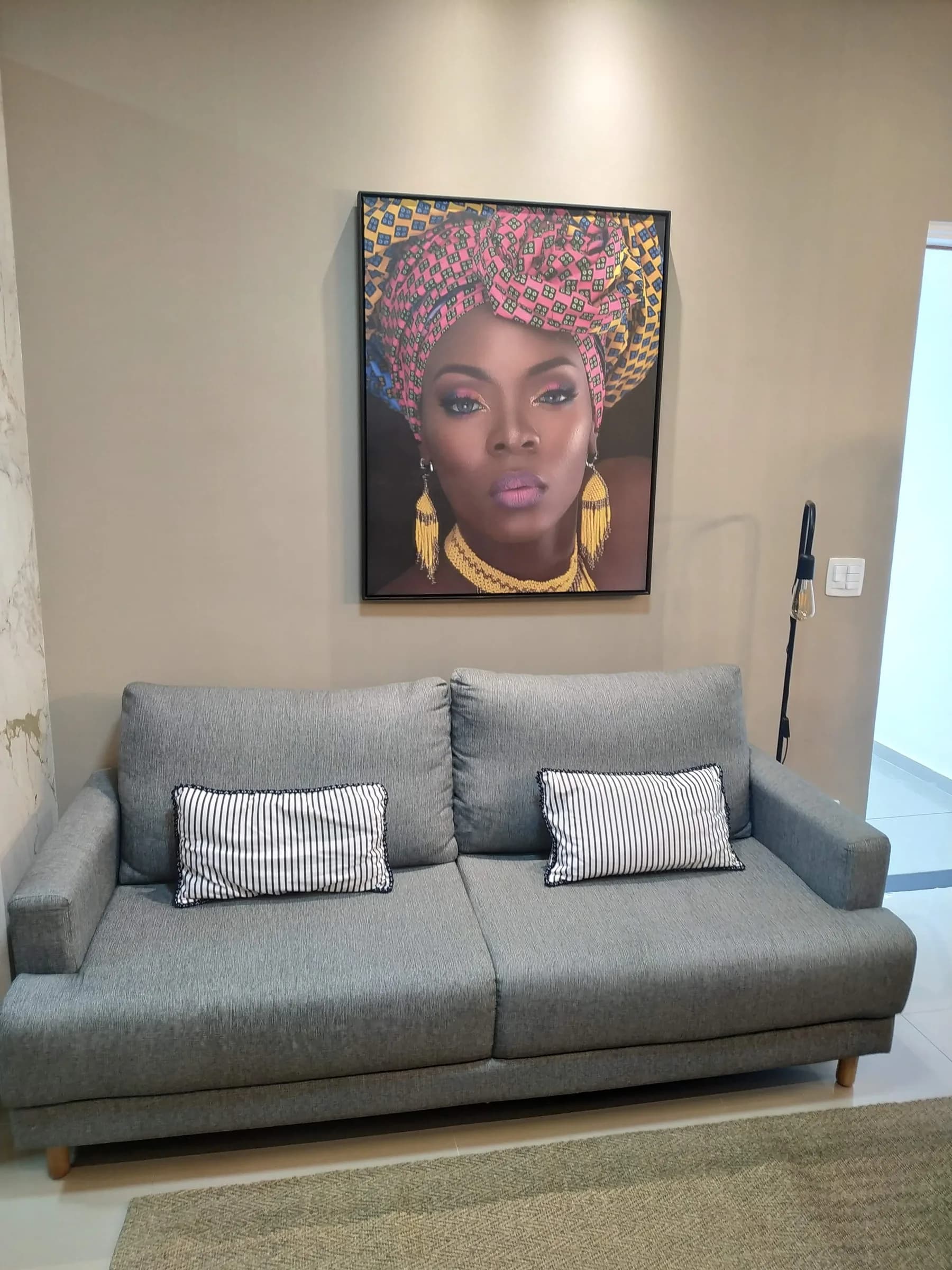 Sofá cinza com almofadas listradas sob retrato de mulher com turbante estampado