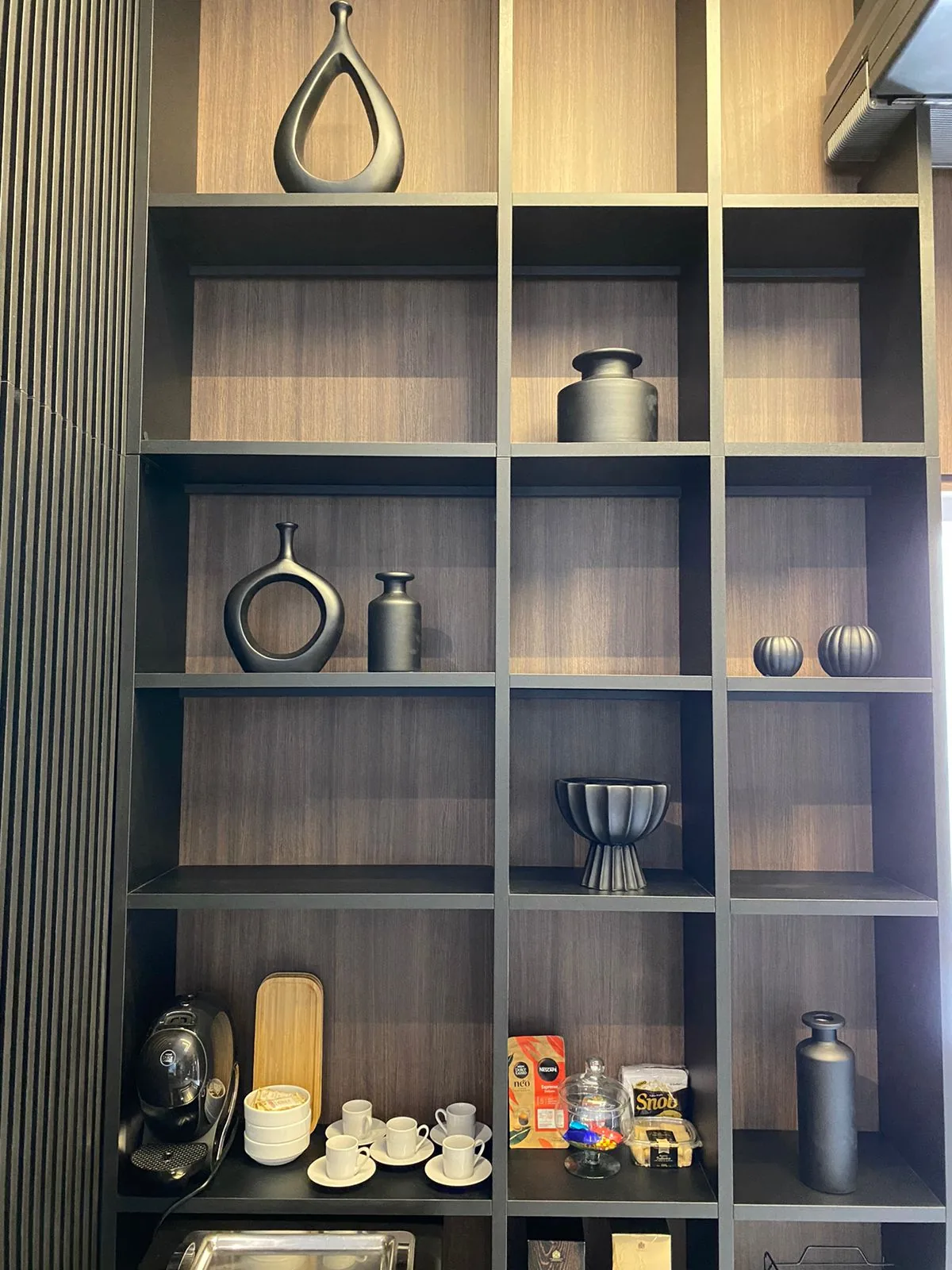 Nichos de madeira escura com vasos pretos, xícaras e cafeteira na prateleira