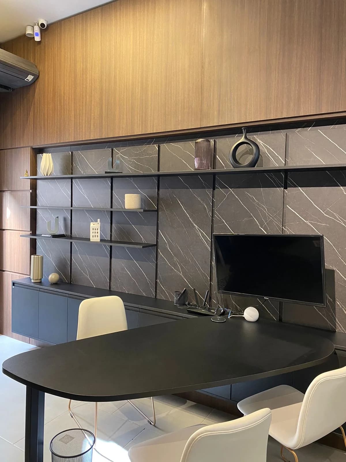 Escritório com painel marmorizado, prateleiras com objetos e mesa preta orgânica